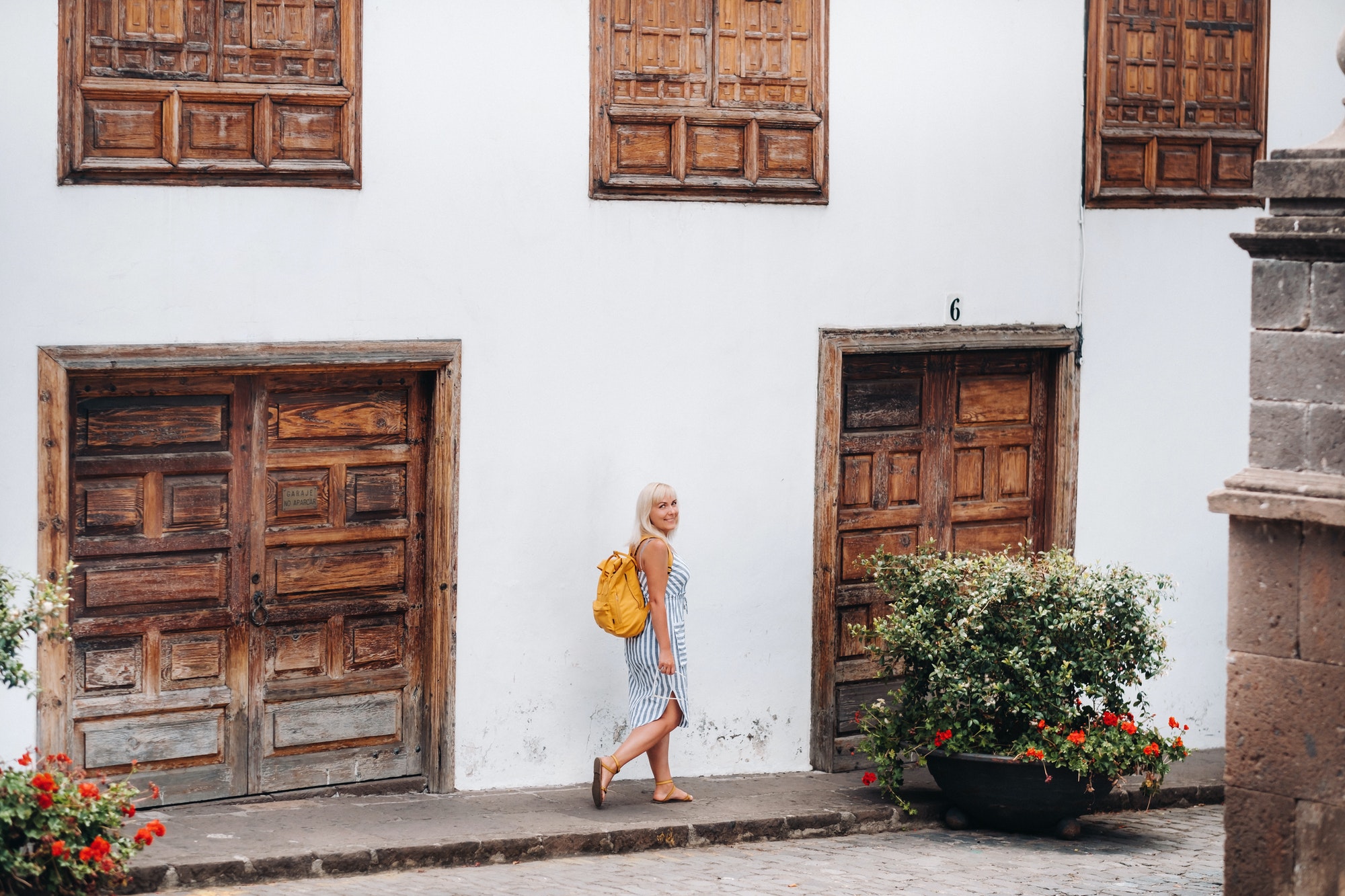 a blonde in a sundress with a backpack walks along the street of the Old town of Garachico on the